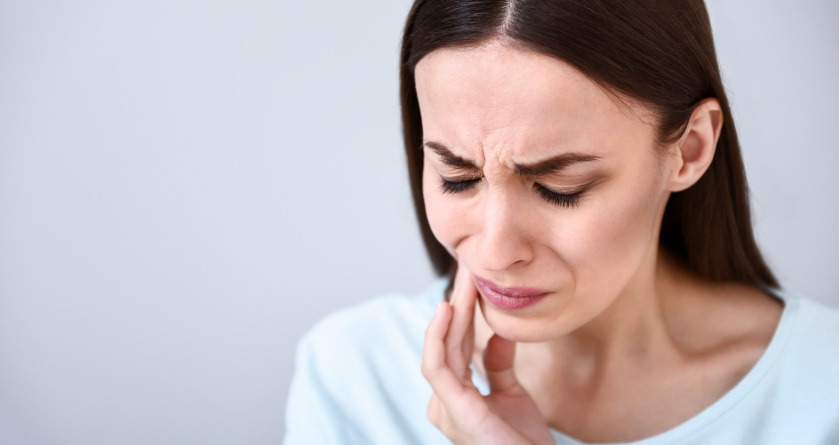 brunette woman against gray background holding mouth wincing in pain