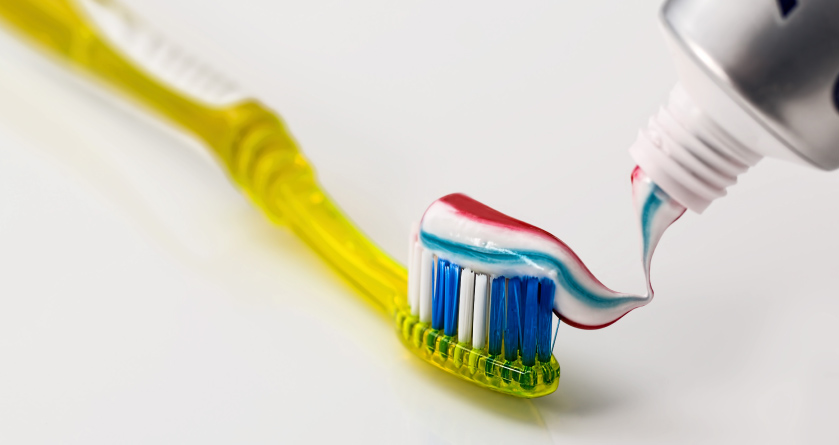 A yellow toothbrush with toothpaste being squeezed onto it