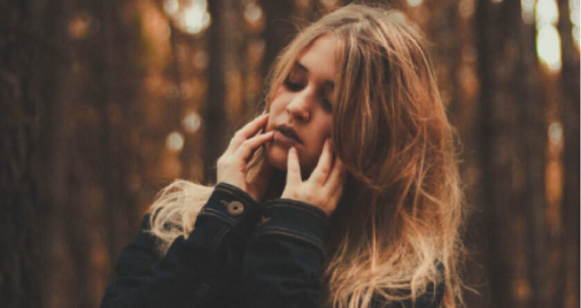 girl with brown hair wearing a coat holding her jaw with both hands