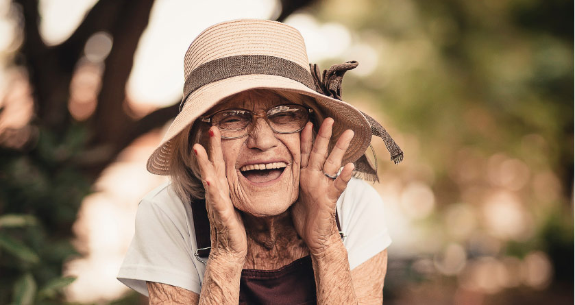 elderly woman wearing a straw hat calling out with hands at the side of her face