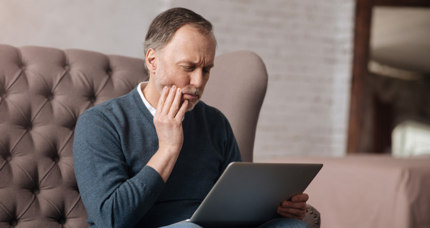 man looking at a laptop holding his jaw in pain from gum disease