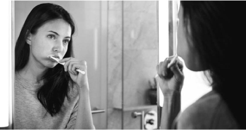 girl looking in the bathroom mirror brushing her teeth