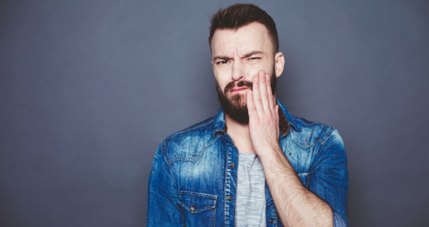 bearded man wearing a denim jacket holds his jaw wondering if gum recession is reversible