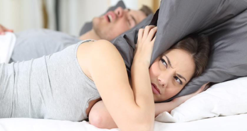 woman covering her ears with a pillow to block out her partners snoring from sleep apnea