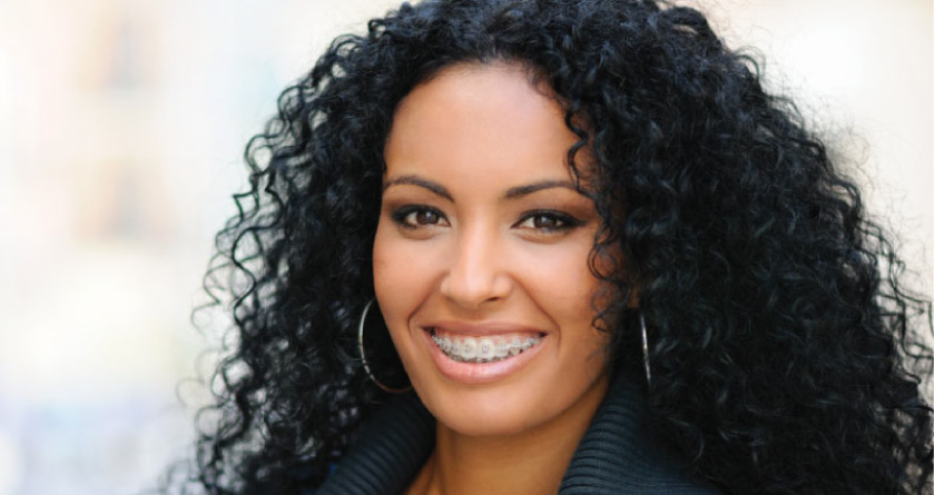 woman with dark curly hair smiles showing off her braces