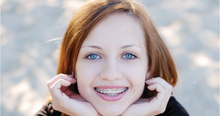 girl with red hair and blue eyes smiles showing off her orthodontics