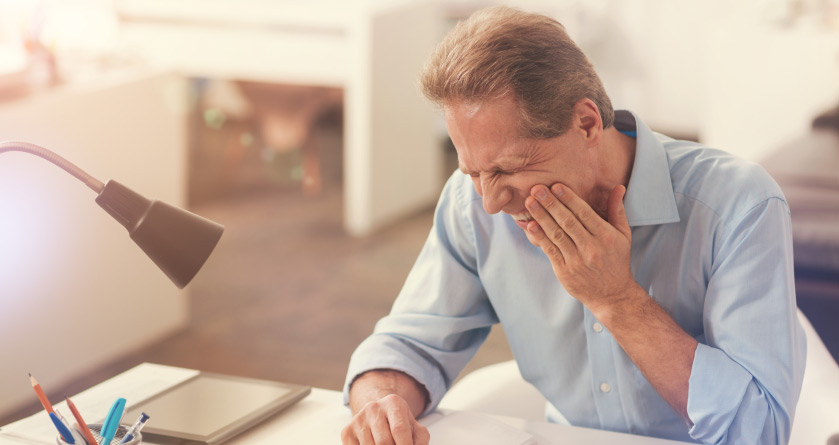 man sitting at a desk holding his jaw in pain from a failing dental implant