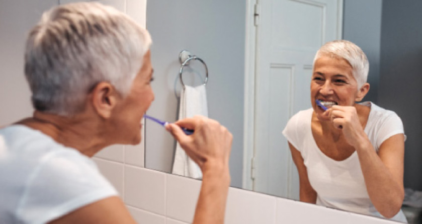 woman brushing her teeth in the bathroom mirror to fight plaque buildup