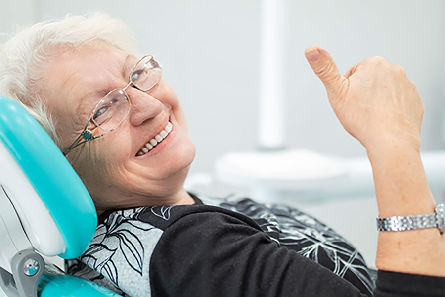 senior woman sitting in the dentist's chair gives a thumbs up after an oral cancer screening