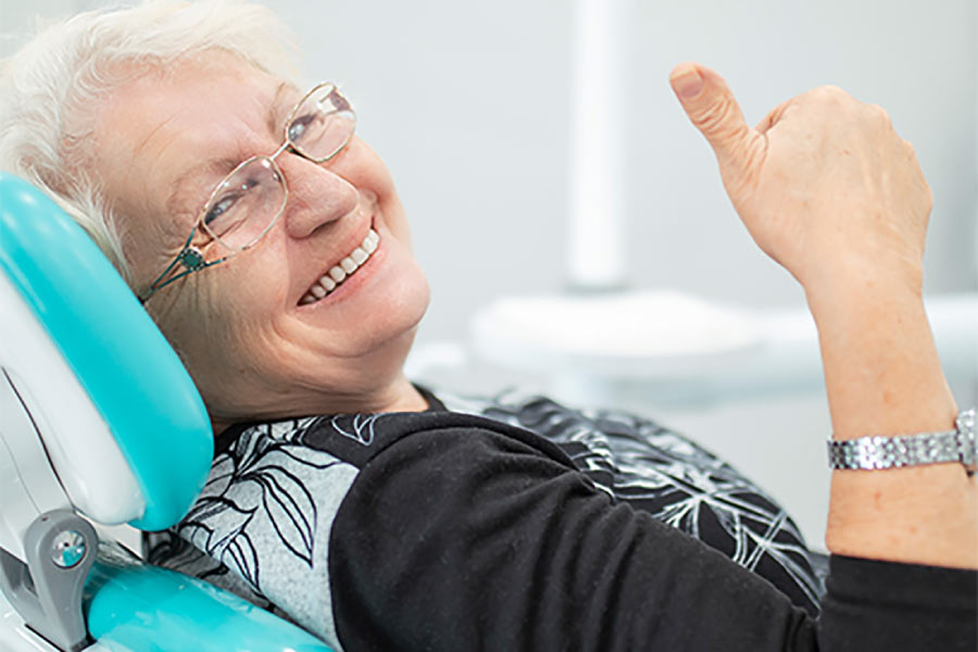 senior woman smiles and gives a thumbs up after successful dental repairs