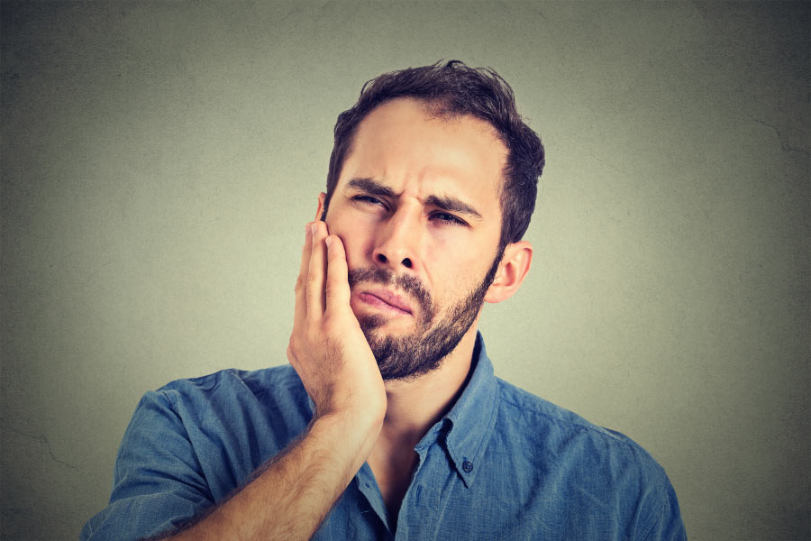 bearded man holds his jaw with painful gums