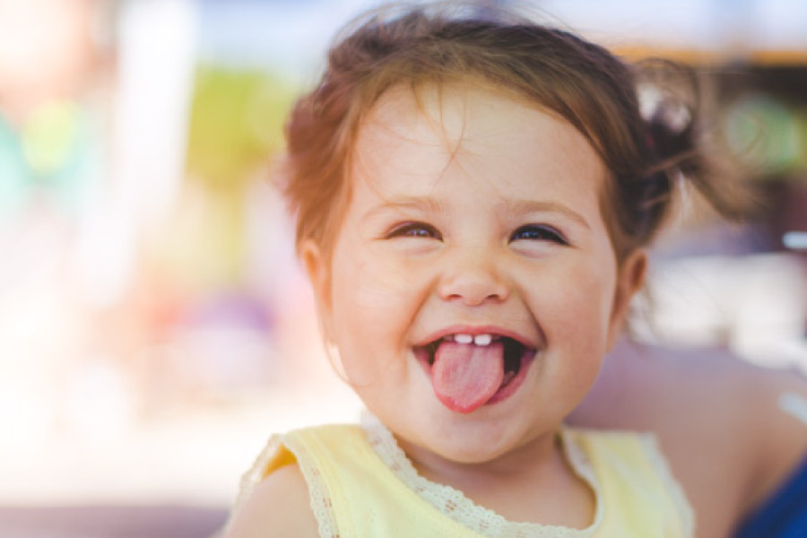 baby girl sticking out her tongue showing off two baby teeth