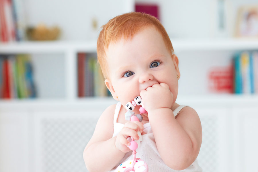 red head baby sucks on a teething toy