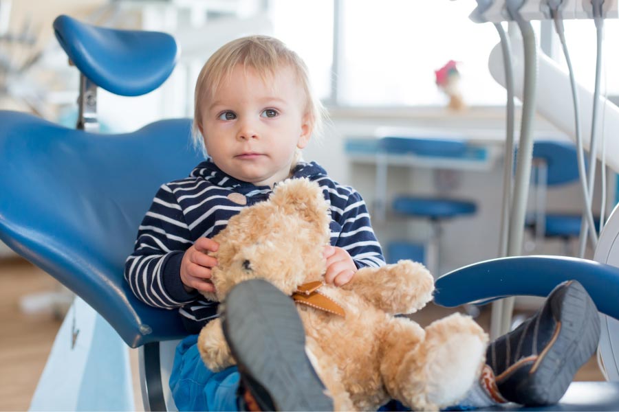 young boy sitting in the dentist chair with a stuffed bear toy
