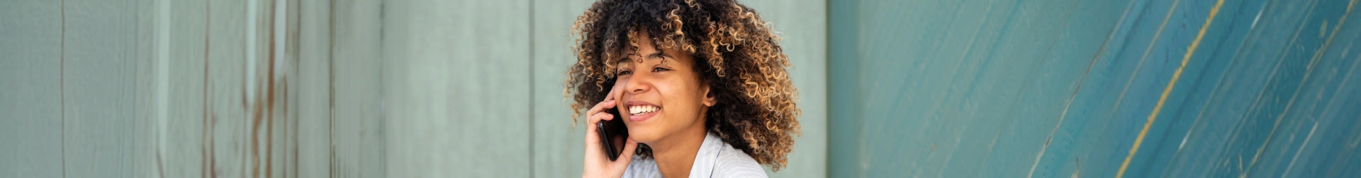Woman with curly hair smiling, wearing headset in modern dental office setting.